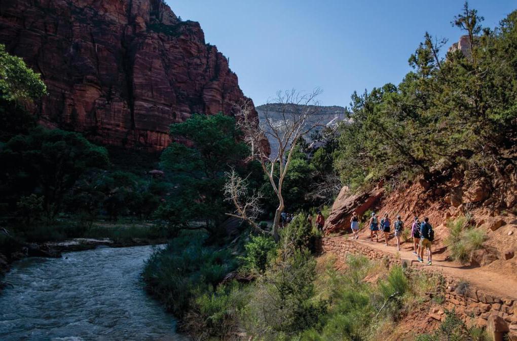 Students walk along a trail in a small canyon with a river flowing not far below them